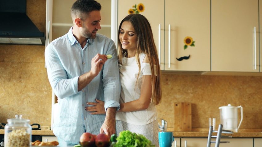 Happy young couple in the kitchen. Handsome man meet and feed his girlfriend early morning at home